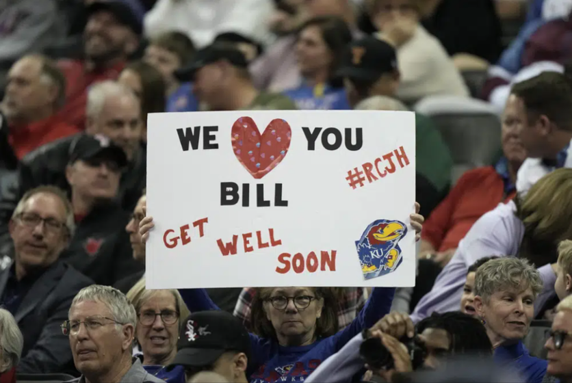 A fan holds up a get well sign for Kansas head coach Bill Self during the first half of an NCAA college basketball game against West Virginia in the second round of the Big 12 Conference tournament Thursday, March 9, 2023, in Kansas City, Mo.
